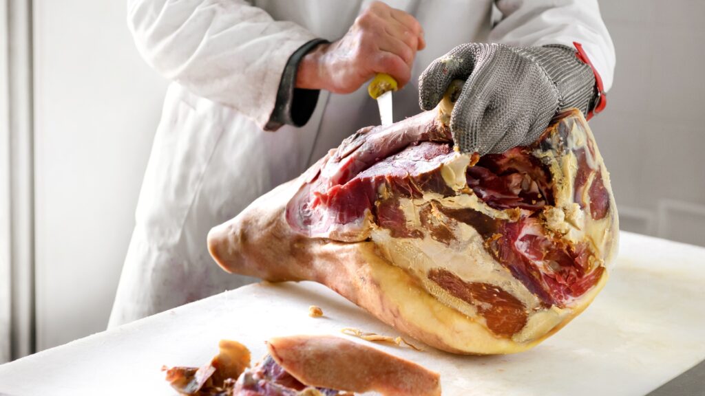 Butcher works on ham, using metal glove